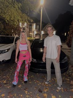 a man and woman standing next to a car in front of a house at night