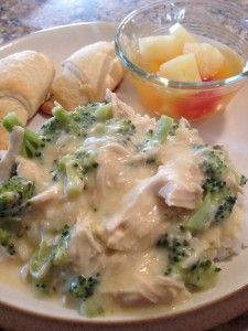 a white plate topped with chicken and broccoli covered in gravy next to croissants