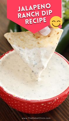 a hand holding a tortilla chip over a bowl filled with ranch dip sauce