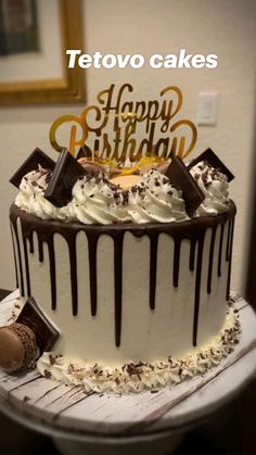 a birthday cake with white frosting and chocolate drizzled on top is sitting on a table