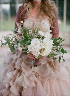 a woman holding a bouquet of flowers in her hand and wearing a dress with ruffled layers