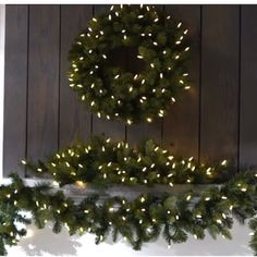 a wreath and garland on a mantle with christmas lights hanging from the top, in front of a wood paneled wall