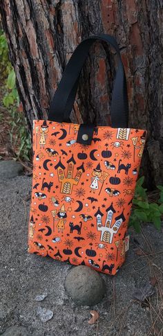 an orange and black tote bag sitting next to a tree with halloween decorations on it