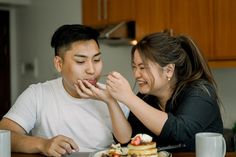 a man and woman sitting at a table with food in front of them, smiling