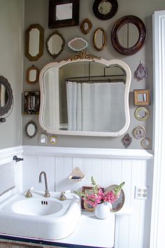 a white sink sitting under a bathroom mirror next to a wall with mirrors on it