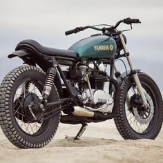 a green yamaha motorcycle parked on top of a sandy beach