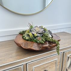 a wooden bowl with succulents and other plants on it sitting on top of a dresser