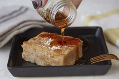 a person pouring syrup on top of a piece of cake in a black square plate