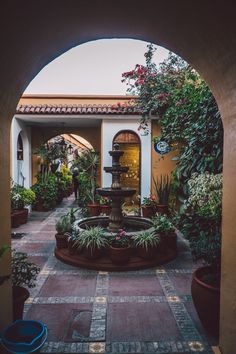 an archway leading into a courtyard with potted plants and a fountain in the center