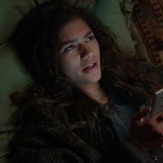 a woman laying in bed holding a remote control and looking at her cell phone screen