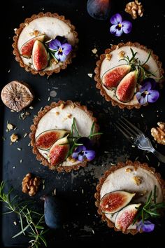 four pies with flowers and nuts on a black surface next to a knife, fork and spoon