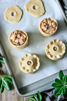 four small pastries on a baking sheet with leaves around them and one is filled with sauce