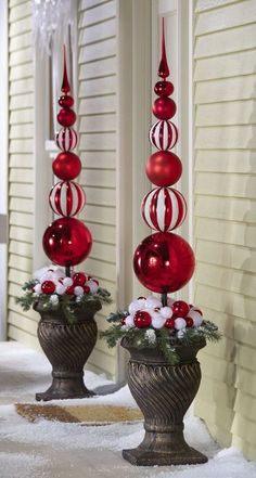 two red and white ornaments are in vases on the snow covered ground next to a house