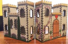 two cardboard castles sitting on top of a wooden table next to each other with doors and windows