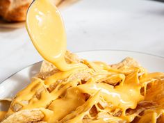 a spoon full of cheese sauce being poured over some tortilla chips on a plate