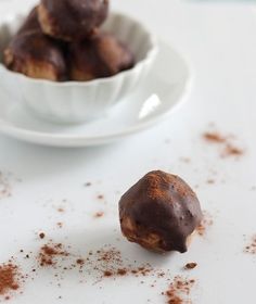 a white bowl filled with chocolate covered doughnuts on top of a table next to a plate