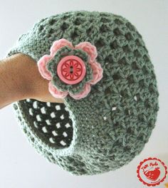 a hand is holding a crocheted hat with a flower on the top and a button in the middle