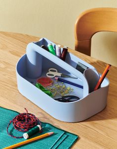 a wooden table topped with a cup filled with pens and pencils next to a pair of scissors