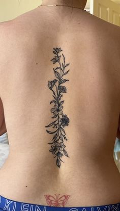 the back of a woman's lower back tattoo with flowers and leaves on it