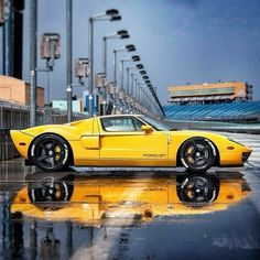 a yellow sports car is parked on the wet pavement in front of an empty stadium