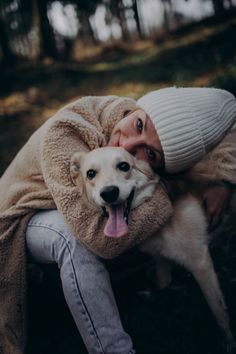 a woman laying on the ground with her dog wrapped in a blanket and smiling at the camera