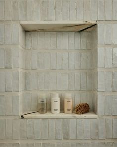 three candles are sitting on a shelf in front of a white brick wall with shelves