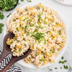 a white bowl filled with macaroni salad next to two bowls of cilantro and parsley