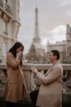 a man kneeling down next to a woman in front of the eiffel tower