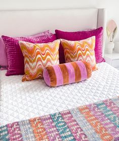 a bed with colorful pillows on top of it and a white headboard in the background