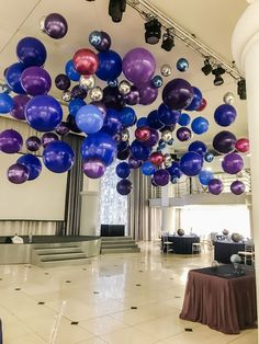 a room filled with lots of purple and blue balloons hanging from it's ceiling