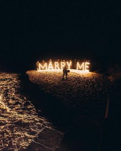 the word marry me is lit up in the dark by two people standing on the beach