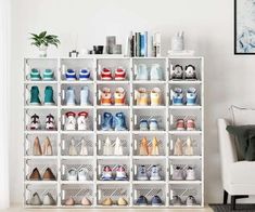 a white shelf filled with lots of pairs of shoes next to a chair and potted plant