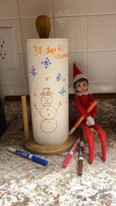 an elf is sitting next to some crayons and a toilet paper roll on the counter