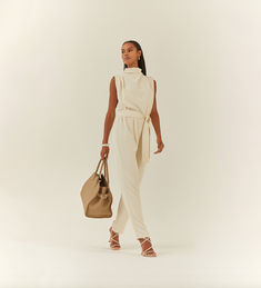 Woman wearing a pearl colored jumpsuit with a high neckline and tie around the waist. She also has a large neutral colored bag. Fitted Jumpsuit, High Neckline, The Day, Dress Up, Jumpsuit