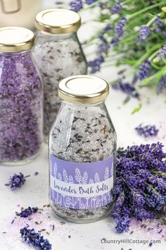 three jars filled with lavender bath salts next to flowers