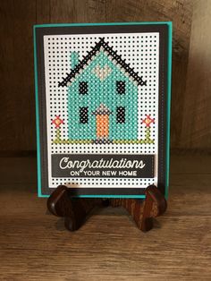 a cross stitch card with the words congratulations on it and a small house in front