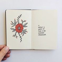 a hand holding an open book with writing on the pages and a red flower in it