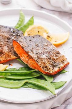 a white plate topped with salmon and green beans next to lemon wedges on a table