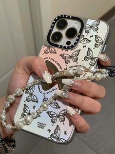 a woman holding up her phone case with butterflies and pearls on the front, while she holds