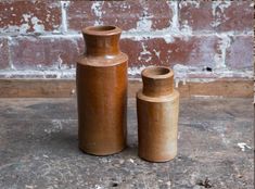 two brown vases sitting next to each other in front of a brick wall