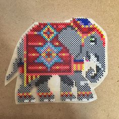 an elephant made out of perler beads on the floor with another elephant standing behind it