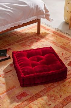 a red square cushion sitting on top of a rug next to a bed with white sheets