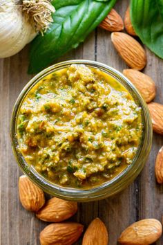 a jar filled with pesto and almonds on top of a wooden table next to green leaves