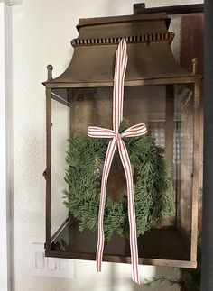 a christmas wreath hanging on the wall in front of an old fashioned light fixture with a ribbon tied around it