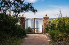 an iron gate leads into the ocean from a path leading to some bushes and trees