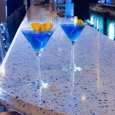 two blue martinis sitting on top of a counter next to each other in front of a bar