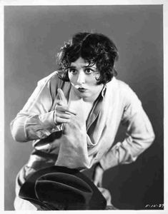 an old black and white photo of a woman with a hat on her head looking at the camera