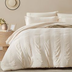 a bed with white comforter and pillows in a room next to a nightstand on the floor