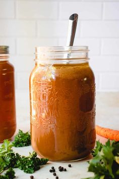 two jars filled with liquid sitting on top of a counter next to carrots and parsley