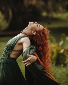 a woman with red hair wearing a green dress and holding her hands out to the side